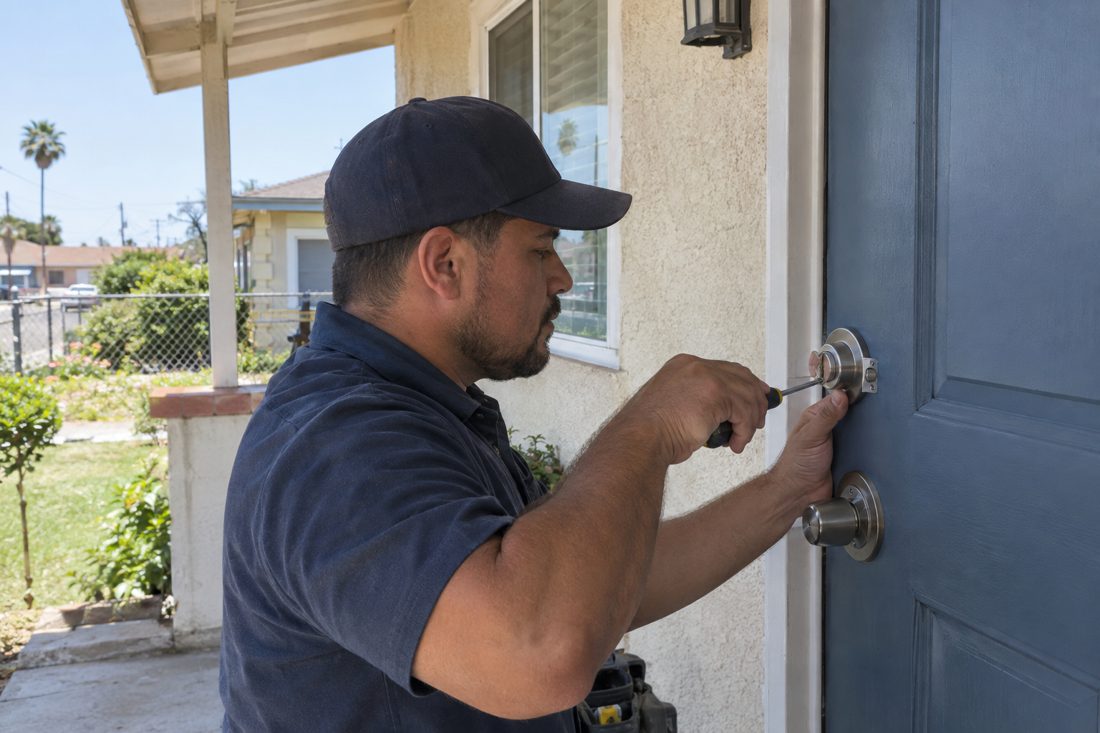 Close view of a locksmith fitting a new deadbolt into the painted front door of a single-story East Compton home in East Compton, CA