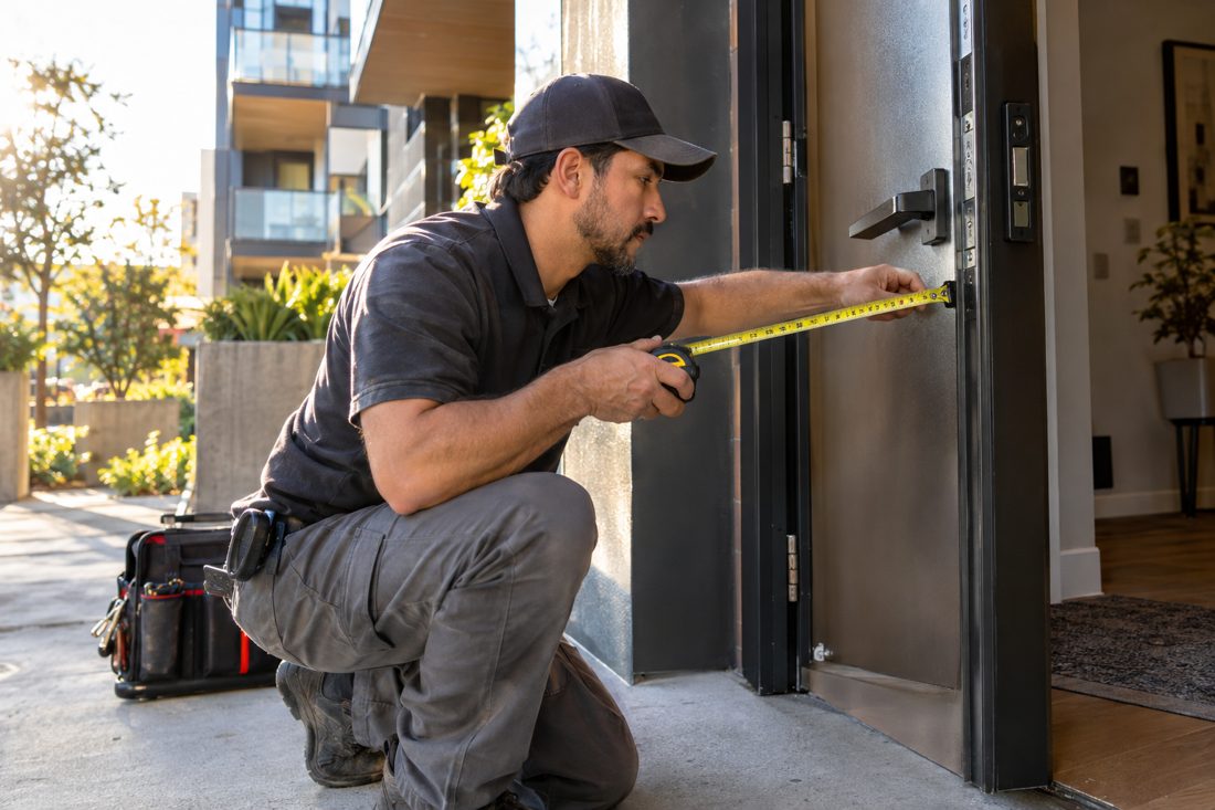 A locksmith measuring a door backset with a tape measure at a modern Culver City condo building entry in Culver City, CA