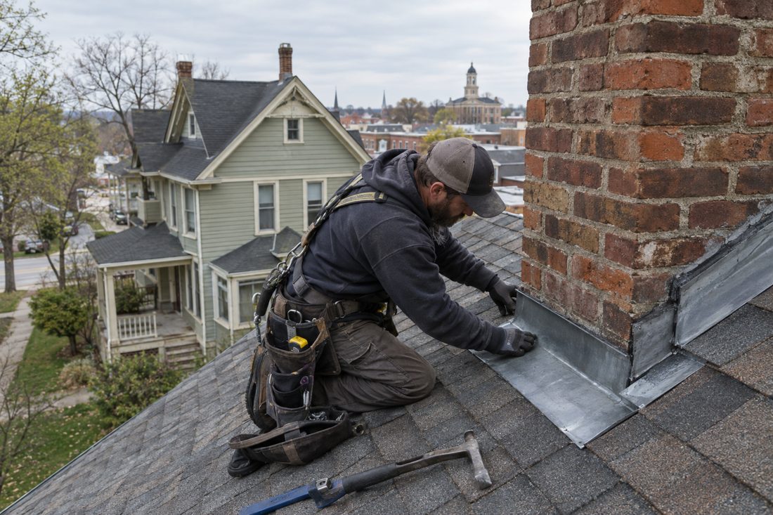 A close view of a roofer checking flashing around a chimney on an older Marion home, with tools resting safely on the roof in Marion, IA