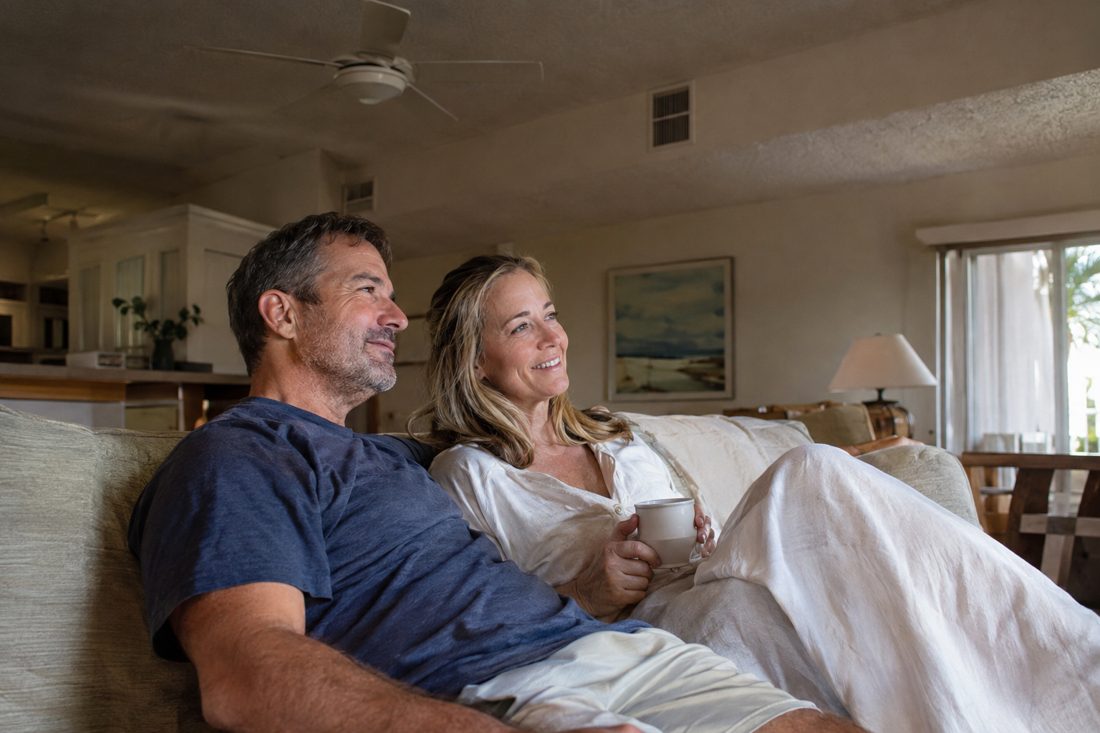 A family relaxing in a cool living room with ceiling fan and vents at a 1970s low-rise condo building in Boynton Beach, FL